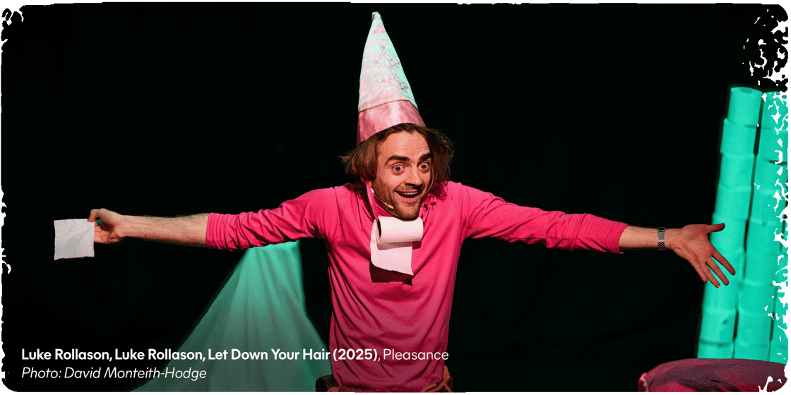 A smiling Fringe performer wearing a pink outfit and a pointy hat with a toilet-roll dangling under their chin, gesturing widely onstage. Credit text: 'Luke Rollason, Luke Rollason, Let Down Your Hair (2025), Pleasance. Photo: David Monteith-Hodge.'